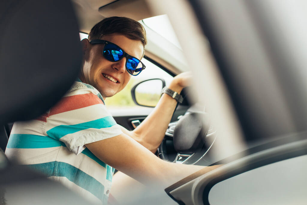 Hezký mladý muž ve slunečních brýlích, usměvavý muž řídí své nové auto, usmívá se při řízení, úspěch v pohybu - Fotografie, Obrázek