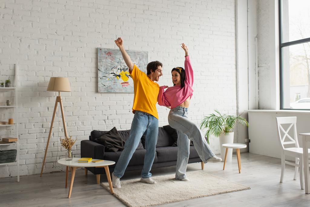 sorrindo jovem casal em roupas casuais dançando na sala de estar - Foto, Imagem