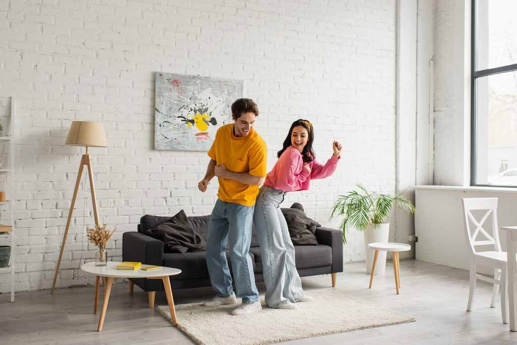 позитивна молода пара в повсякденному одязі танцює у вітальні
 - Фото, зображення