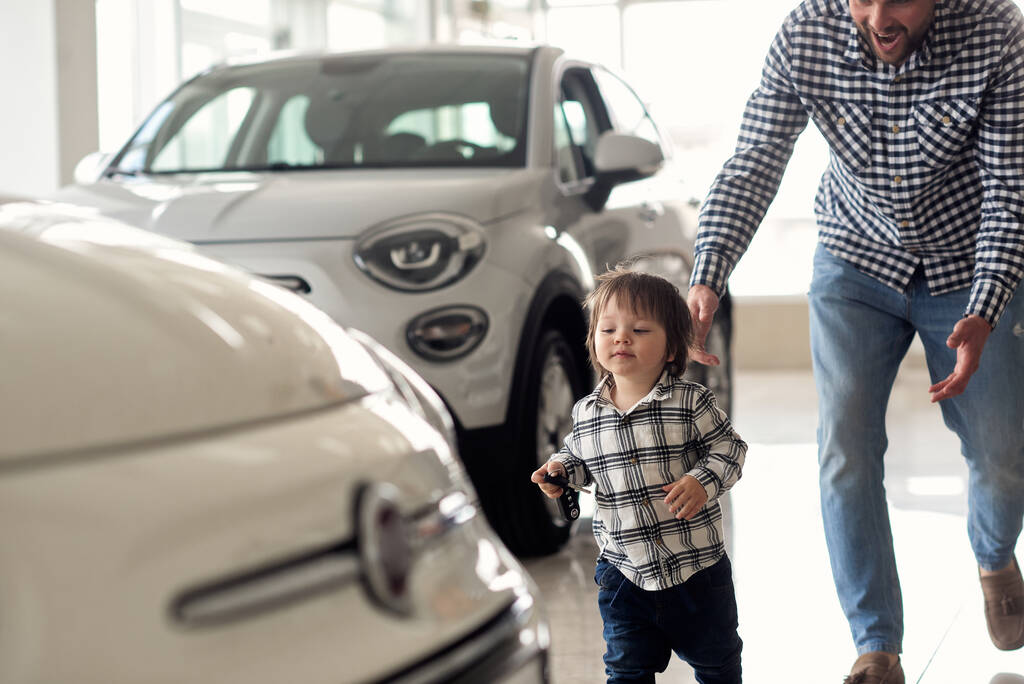 Πατέρας και γιος με τα πόδια γύρω από το μεγάλο αυτοκίνητο δείχνουν και να εξετάσει νέα μοντέλα αυτοκινήτων. - Φωτογραφία, εικόνα