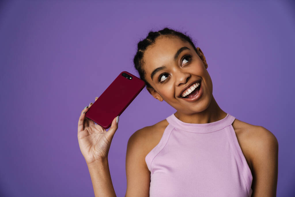 Giovane donna nera sorridente e tenendo il telefono cellulare isolato su sfondo viola - Foto, immagini