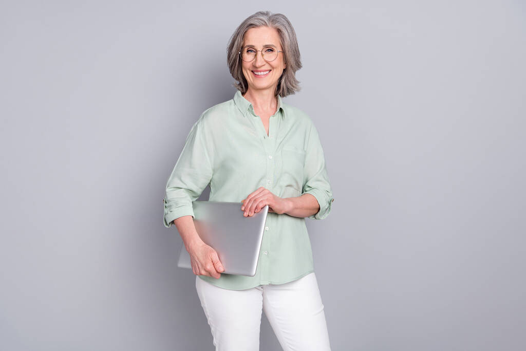 Zdjęcie dojrzałej uśmiechniętej pięknej inteligentnej bizneswoman trzymać laptopa odizolowany na szarym tle koloru - Zdjęcie, obraz