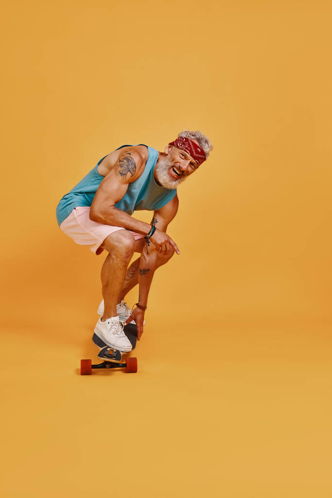オレンジの背景を持つアクティブなシニア男性スケートボードのフル長さ - 写真・画像