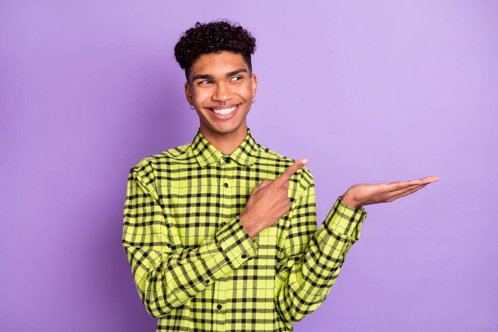 Ritratto di attraente ragazzo allegro che tiene su palmo dimostrando spazio copia isolato su sfondo viola viola - Foto, immagini