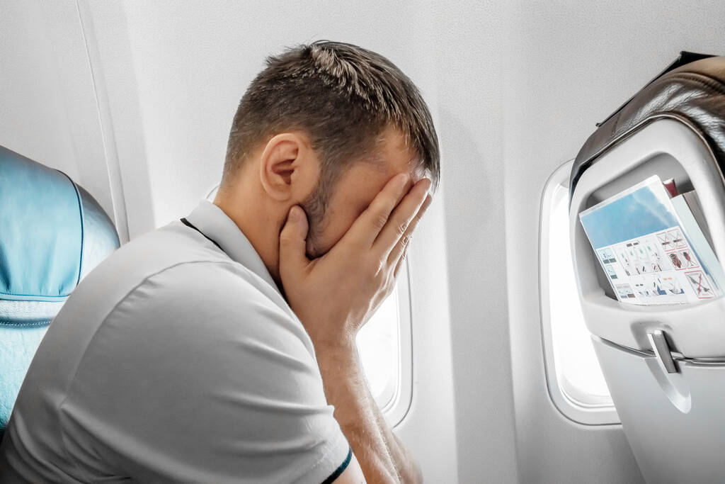 Un hombre se sienta frente a una ventana de avión y está nervioso, temeroso de volar, la cabina de un avión de pasajeros. Aerofobia, fobilya, vuelos internacionales - Foto, Imagen
