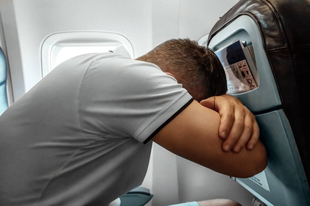Een man zit voor een vliegtuigraam en is nerveus, bang om te vliegen, de cabine van een passagiersvliegtuig. Aerofobie, fobilya, internationale vluchten - Foto, afbeelding