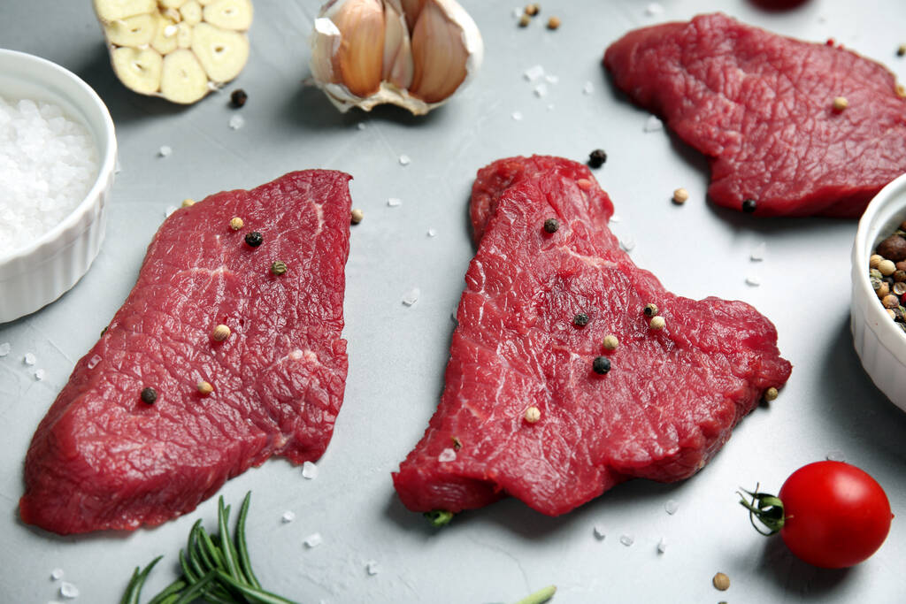 Vers rauw vlees steaks en specerijen op lichtgrijze tafel - Foto, afbeelding