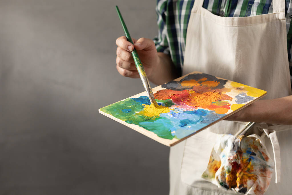 Malíř drží paletu s barvou štětcem. Mladý umělec a malířství štětcem v kreativním studiu - Fotografie, Obrázek