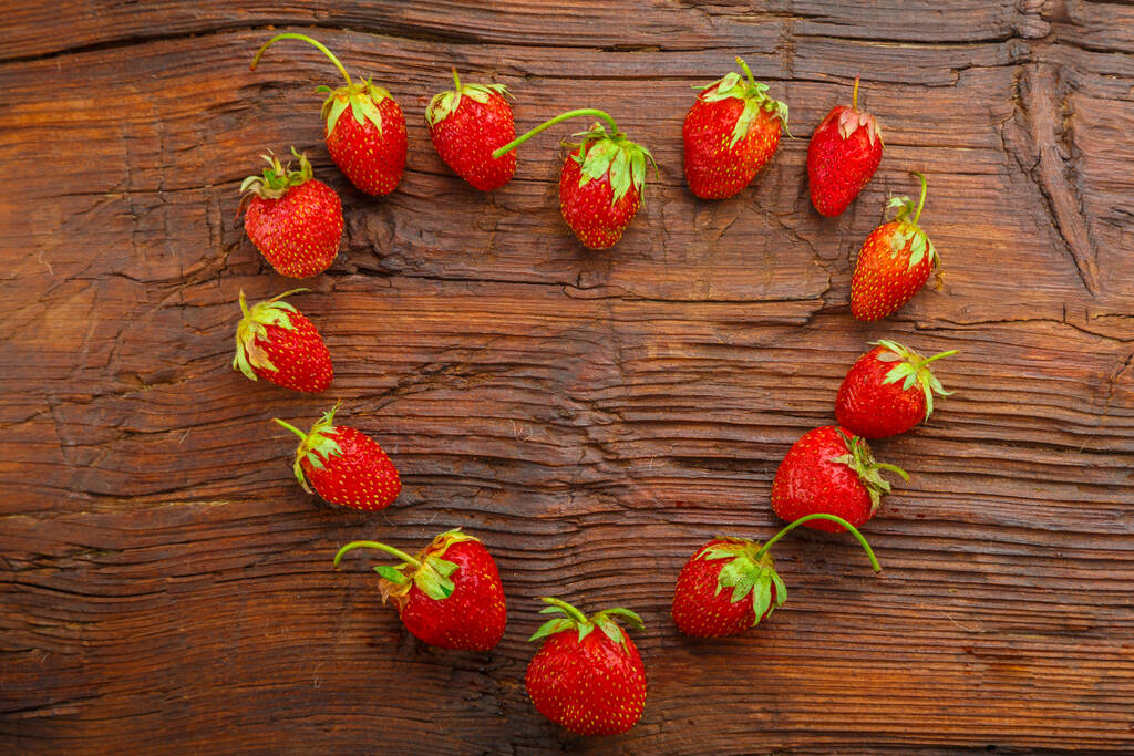 Fresh strawberries on a wooden background are laid out in the shape of a heart. - Photo, Image
