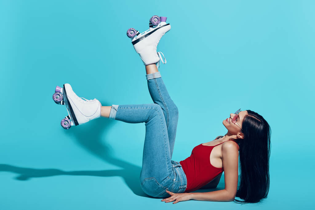 Atractiva joven mujer con patines y sonriendo tumbada sobre fondo azul - Foto, Imagen