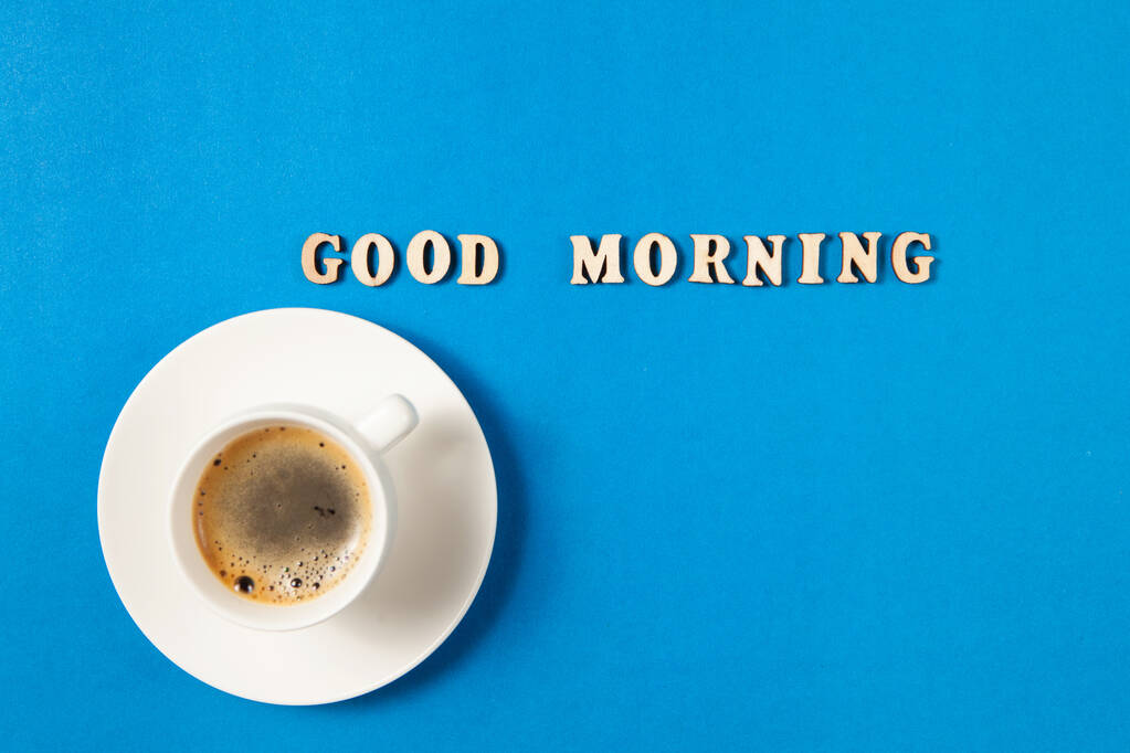 Bir fincan sade kahve ve mavi arkaplandaki ahşap harflerden günaydın mesajı. Yeni bir günün başlangıcının konsept fotoğrafı. Pankart veya blog için düz dizayn kavramını kabul et. - Fotoğraf, Görsel