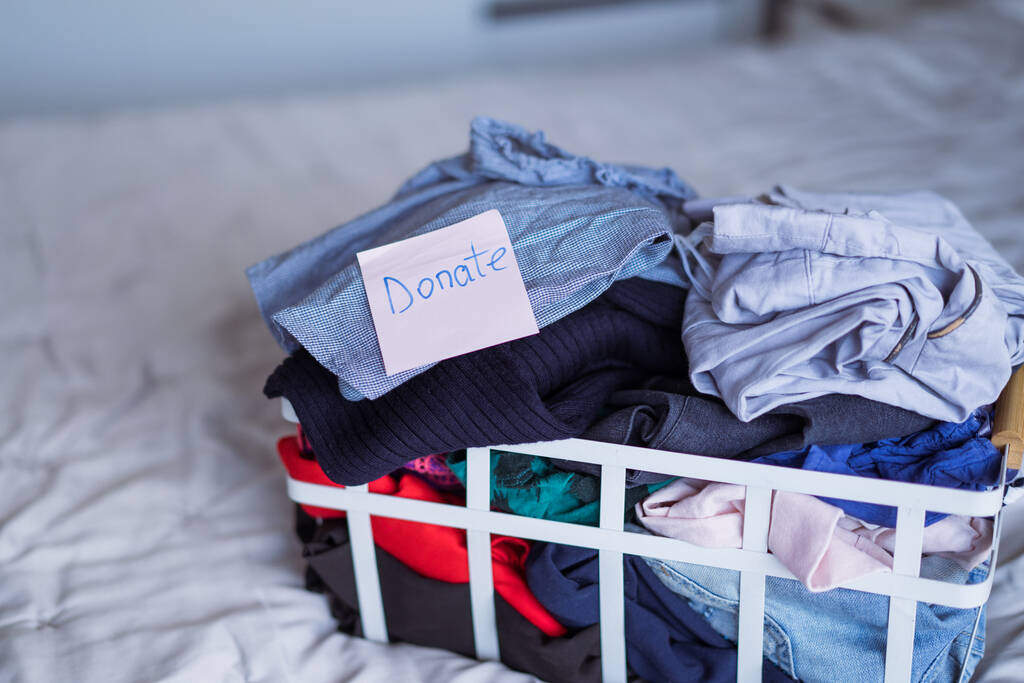 Una canasta de ropa seleccionada para donar a una tienda de caridad de pie en la cama. Decluttering Ropa, Clasificación, y Limpieza. Reutilización, de segunda mano. Consumidor consciente, sostenibilidad - Foto, Imagen