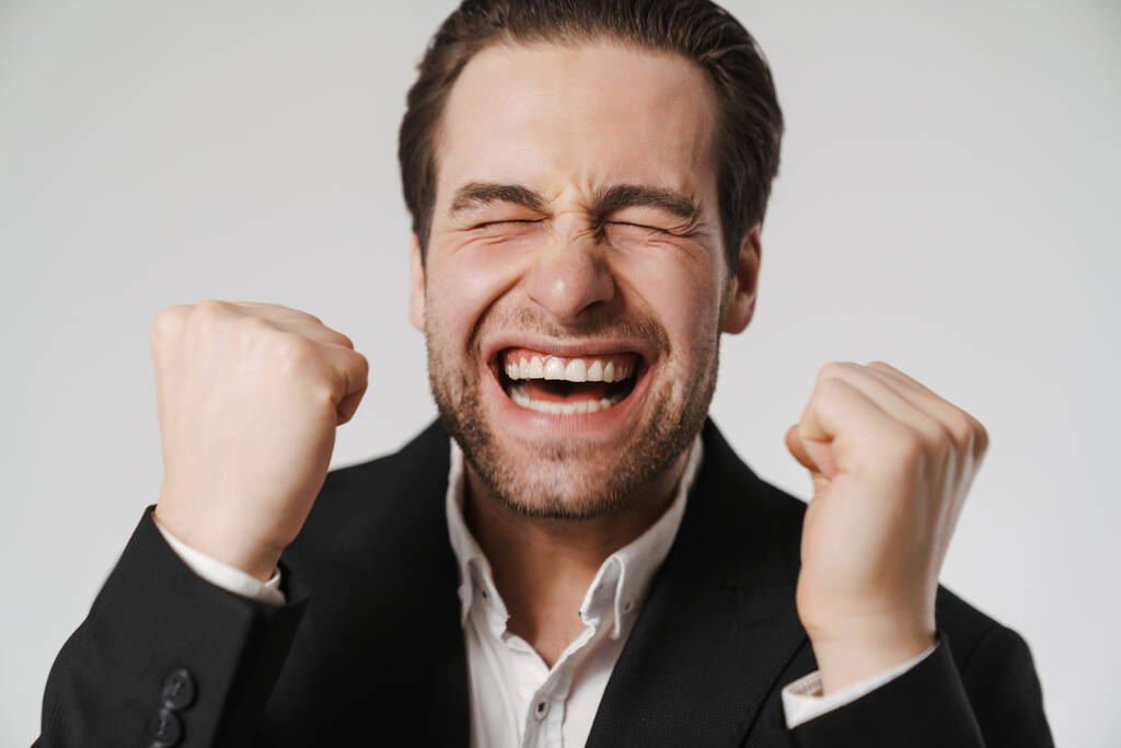 Ξυρισμένος ενθουσιασμένος άντρας με σακάκι ουρλιάζοντας και κάνοντας την κίνηση του νικητή απομονωμένη σε λευκό φόντο - Φωτογραφία, εικόνα