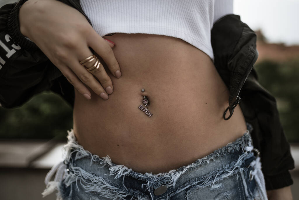 Un primer plano de una barriga femenina con un piercing en el ombligo - Foto, imagen