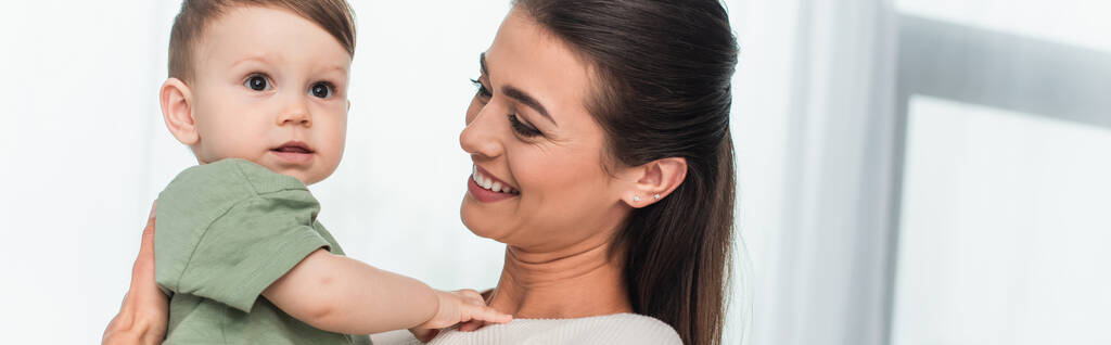 Junge Frau lächelt, während sie ein Kleinkind hält, Transparent  - Foto, Bild