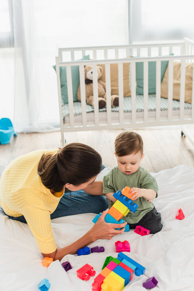 Overhead view of mother holding building blocks near toddler son on bed  - Photo, Image