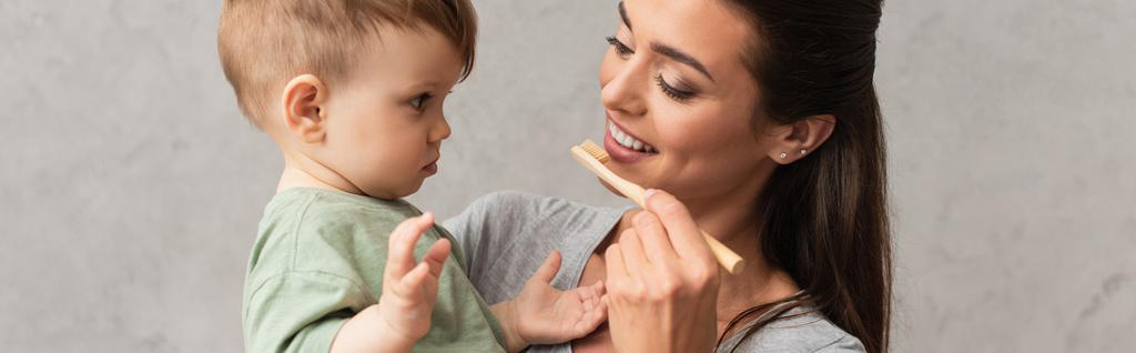 Νεαρή μητέρα με οδοντόβουρτσα κοιτάζοντας το γιο, πανό  - Φωτογραφία, εικόνα