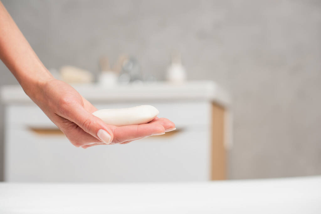 Vista ritagliata della donna che tiene il sapone in bagno sfocato  - Foto, immagini