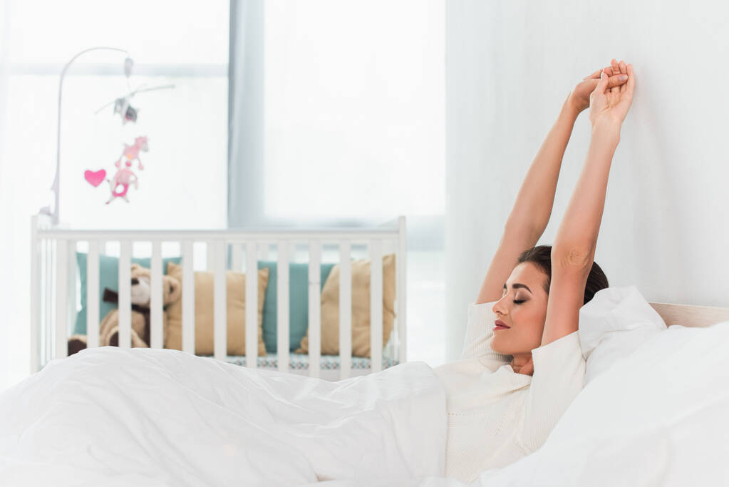Boční pohled na mladou ženu protahování na posteli  - Fotografie, Obrázek