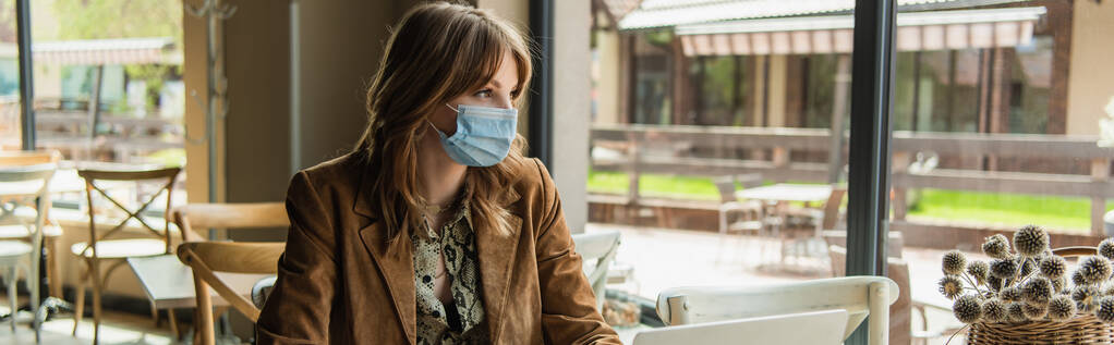 Stilvolle Frau mit medizinischer Maske sitzt neben Laptop im Café, Banner  - Foto, Bild