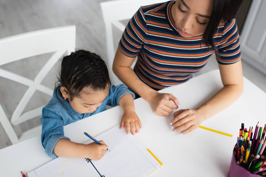 Vue aérienne de l'enfant asiatique dessinant près des crayons de couleur et du parent  - Photo, image