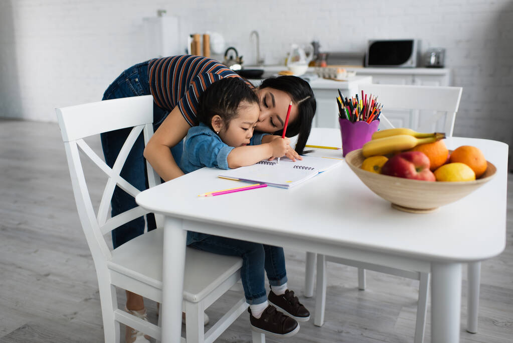 Ασιάτης γονέας φιλιά κόρη σχέδιο στο σημειωματάριο στο σπίτι  - Φωτογραφία, εικόνα
