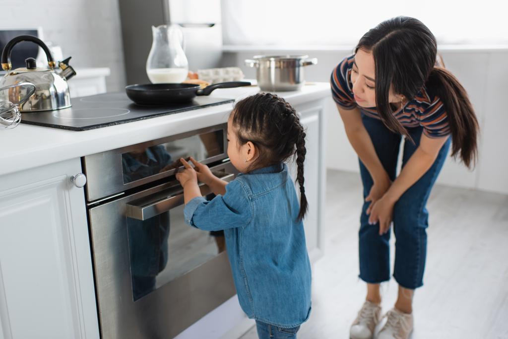 Asiatico bambino toccando display di forno vicino madre in cucina  - Foto, immagini