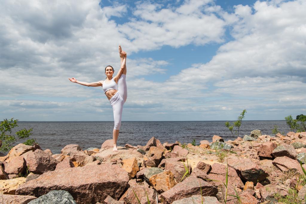 felice donna in abbigliamento sportivo mano in piedi alla posa alluce vicino al mare - Foto, immagini
