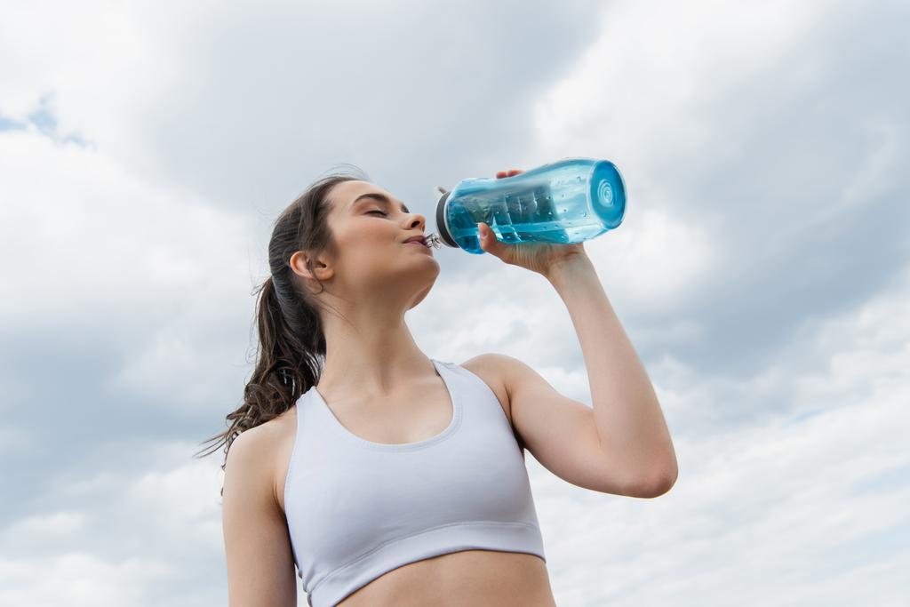 low angle view of brunette woman in crop top drinking water against  sky with clouds - Photo, Image