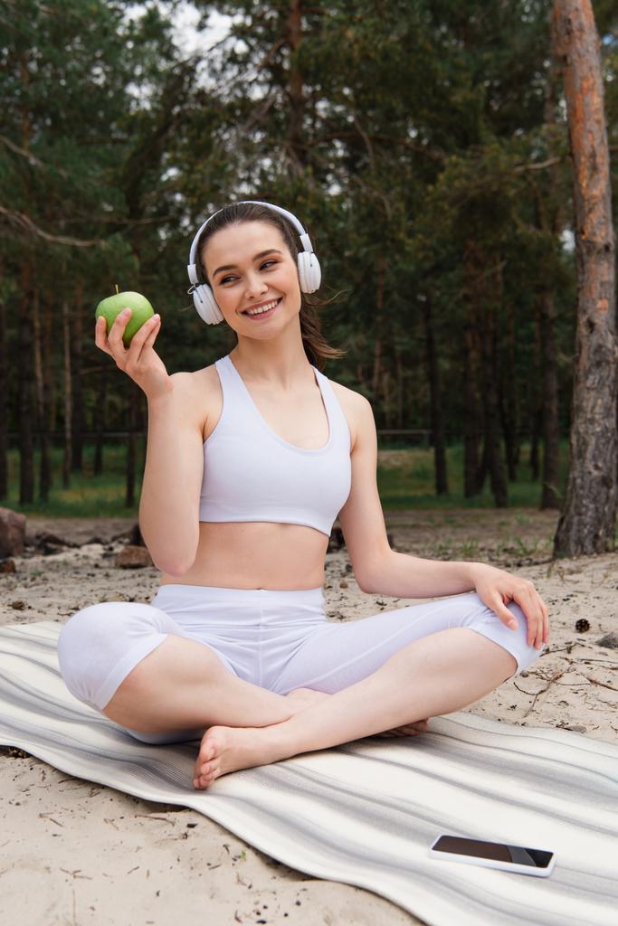 щаслива жінка в навушниках слухає музику, тримаючи яблуко в лісі
 - Фото, зображення