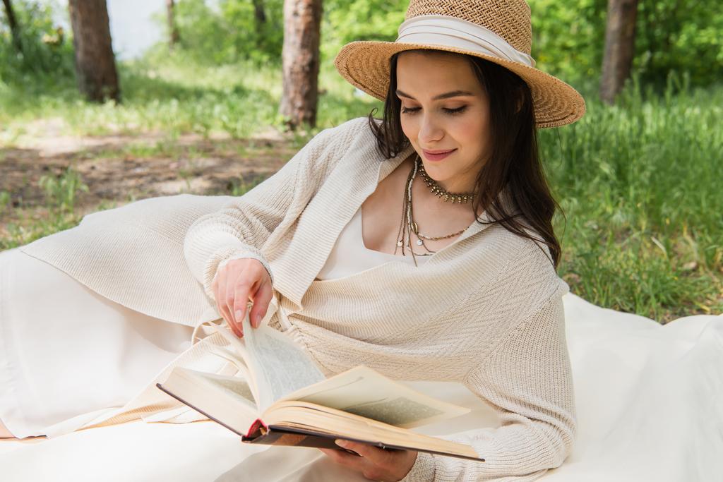 jovem mulher positiva em chapéu de palha leitura romance na floresta - Foto, Imagem