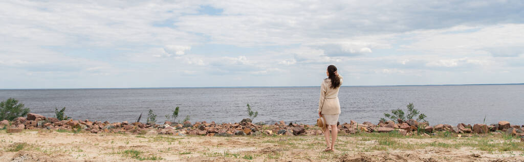日焼け帽子をかぶって海の近くに立っているブルネットの若い女性の完全な長さ、バナー - 写真・画像