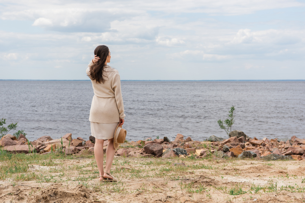 piena lunghezza di bruna donna con cappello da sole e in piedi vicino al mare - Foto, immagini