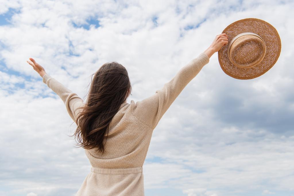 back view of young woman standing with outstretched hands against cloudy sky - Photo, Image