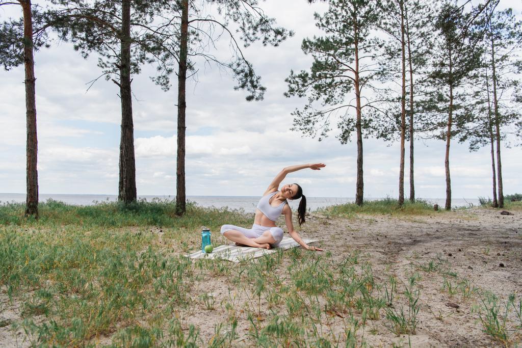 Spor kıyafetli esmer genç bir kadın lotus poz verip yoga minderine uzanıyor.  - Fotoğraf, Görsel