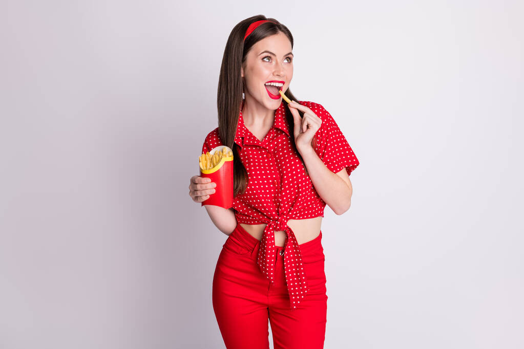 Фото флиртующей девушки держать коробку французский картофель открыть рот смотреть пустое пространство носить красные пунктирные блузки изолированы серый цвет фона - Фото, изображение