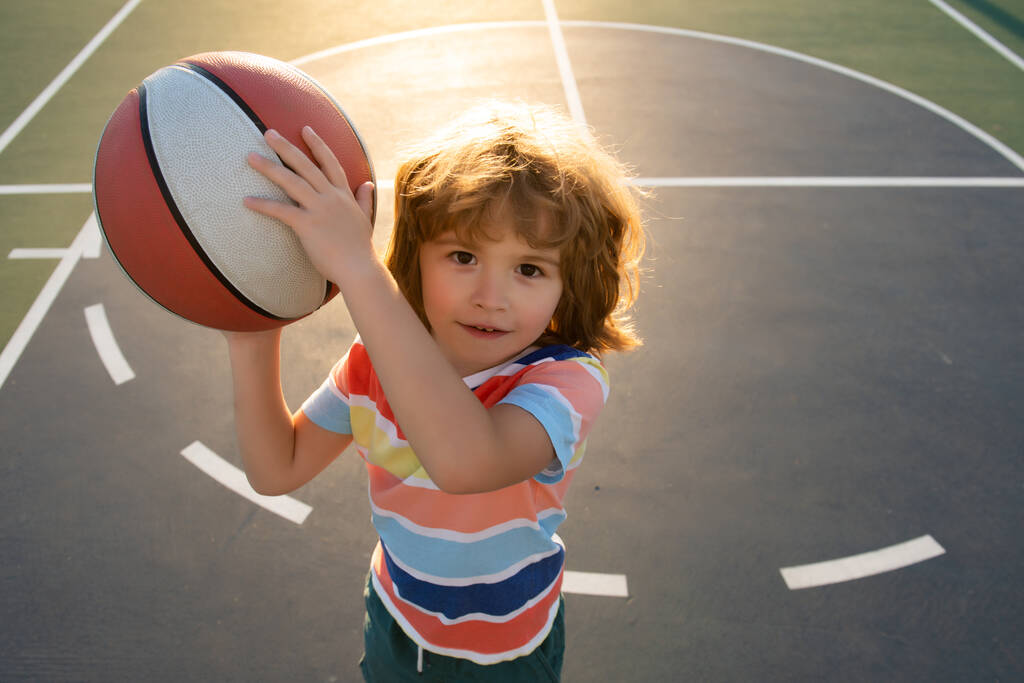 Een kleine blanke sportjongen die basketbalt met een vrolijk gezicht. Portret van een sportief grappig kind. - Foto, afbeelding