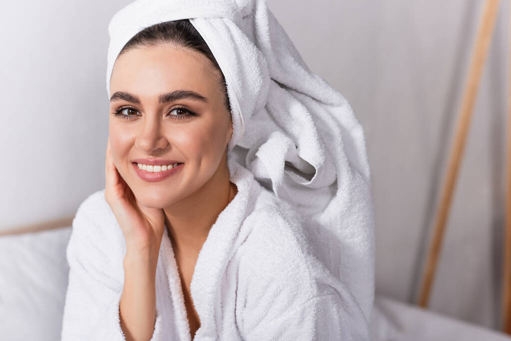 mulher alegre em toalha na cabeça e roupão de banho sorrindo no quarto  - Foto, Imagem