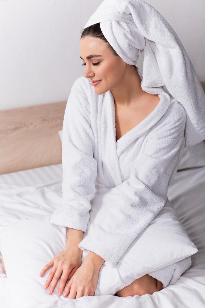 Kafasında havlu ve bornoz olan mutlu kadın yatak odasında oturuyor.  - Fotoğraf, Görsel