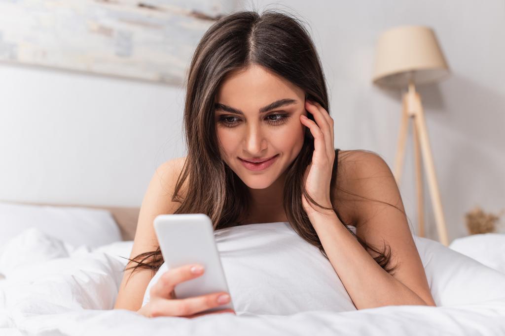 gioiosa giovane donna sdraiata sul letto e utilizzando smartphone  - Foto, immagini