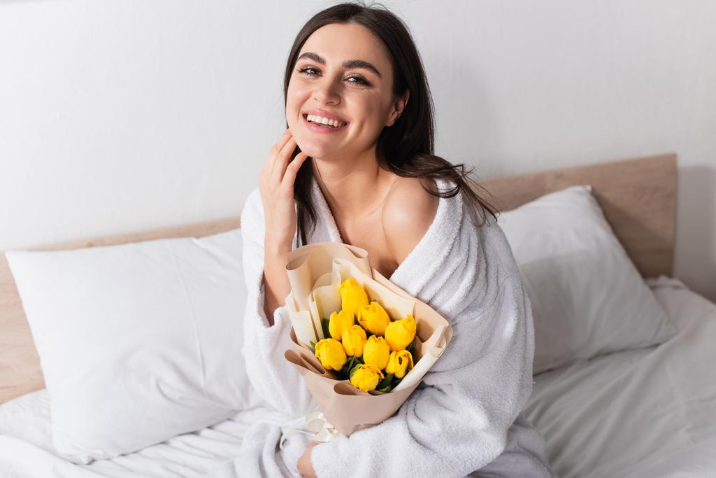 piacere giovane donna in accappatoio in possesso di bouquet di tulipani gialli in camera da letto - Foto, immagini