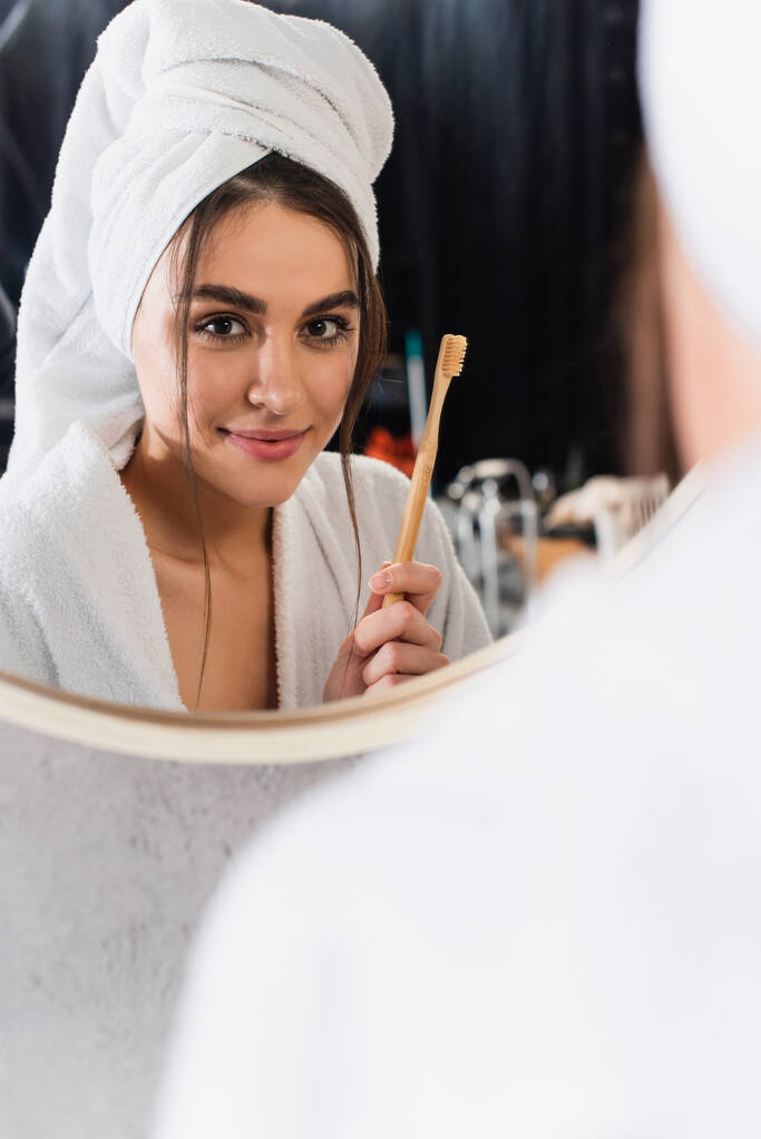відображення жінки в халаті з рушником на голові, що тримає зубну щітку біля дзеркала ванної кімнати
 - Фото, зображення