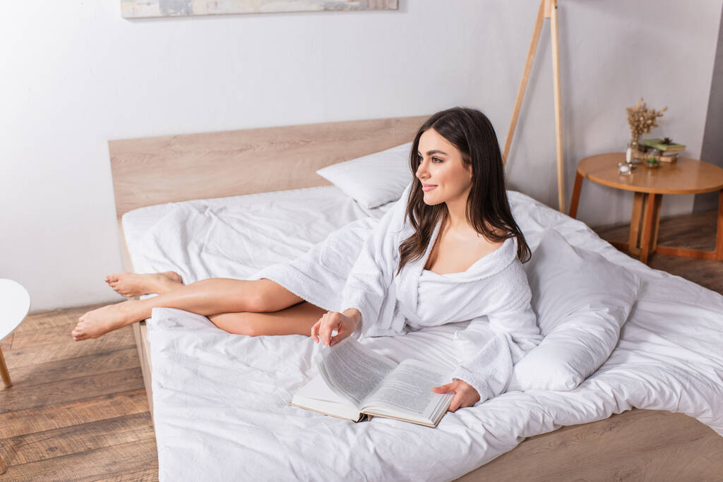 задоволена жінка в халаті лежить на ліжку з книгою
  - Фото, зображення