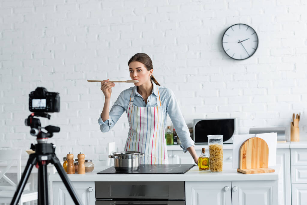 Ev hanımı mutfakta bulanık dijital kamera önünde yemek tadıyor. - Fotoğraf, Görsel