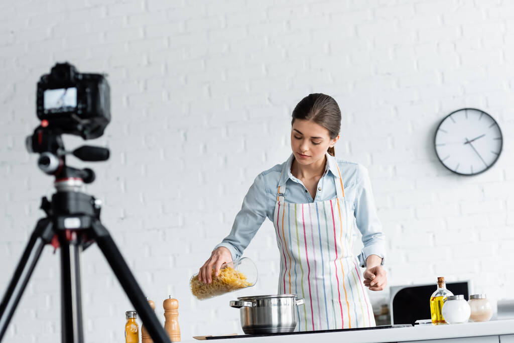 μαγειρικό blogger σε ποδιά προετοιμασία ζυμαρικά μπροστά από θολή ψηφιακή φωτογραφική μηχανή  - Φωτογραφία, εικόνα