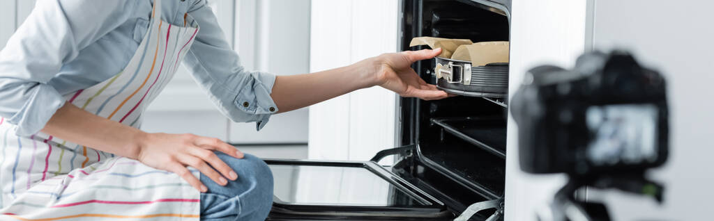 обрезанный вид кулинарного блогера размещение формы выпечки в духовке рядом с размытой цифровой камерой, баннер - Фото, изображение