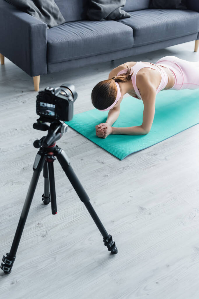 digital camera on tripod near sportswoman training in plank pose on fitness mat - Photo, Image