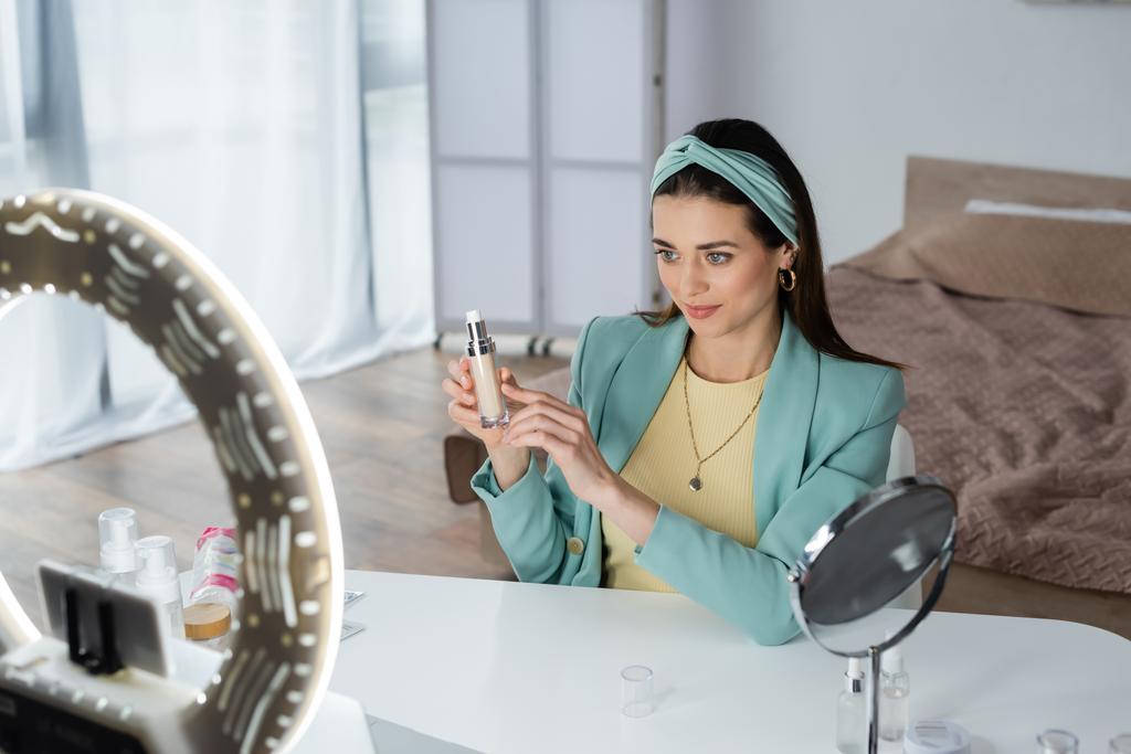 femme élégante pointant vers le fond de teint près du support de téléphone flou avec lampe annulaire - Photo, image