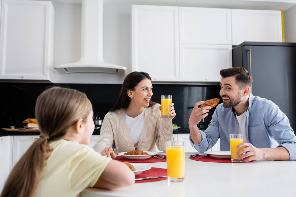 alegre hombre comiendo croissant cerca esposa e hija en borrosa primer plano - Foto, imagen