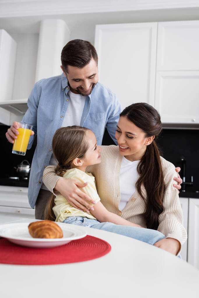 радісна жінка обіймає дочку біля чоловіка з апельсиновим соком на кухні
 - Фото, зображення